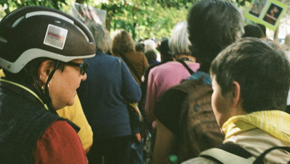 Woman in bike helmet and teenager in crowd walking down tree-lined street