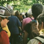 Woman in bike helmet and teenager in crowd walking down tree-lined street