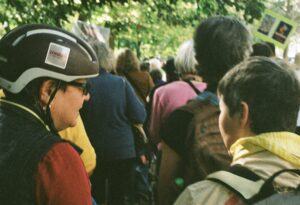 Woman in bike helmet and teenager in crowd walking down tree-lined street